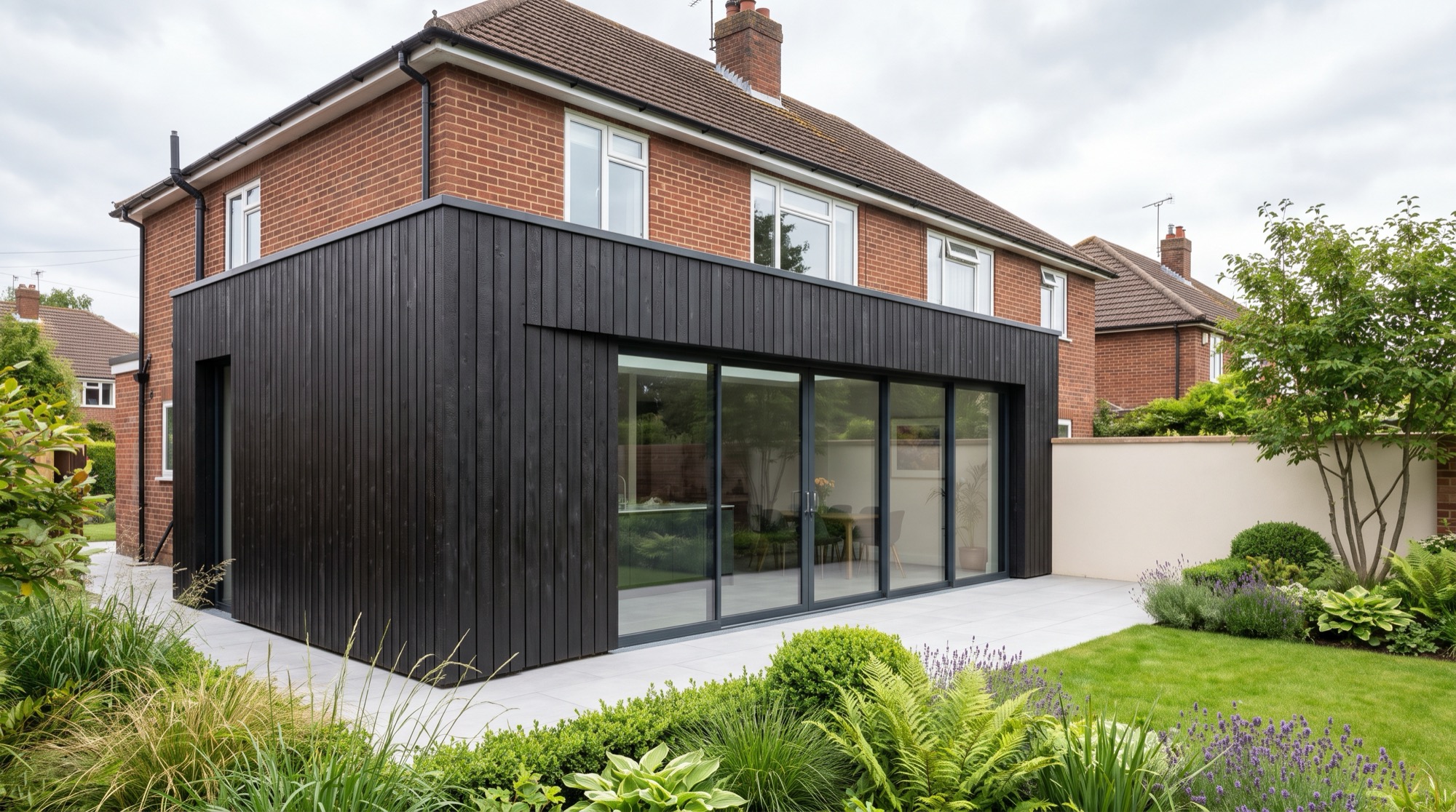 A Nordu extension at the rear of a house, in charred black timber cladding, with full height sliding glazing opening onto a garden.